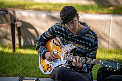 Student playing a guitar. Links to Gifts of Appreciated Securities